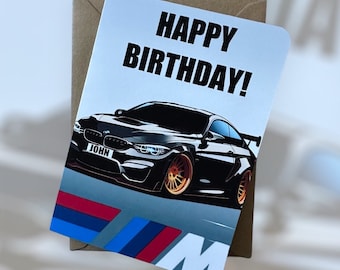 May include: A birthday card with a black BMW M3 car illustration and the text "Happy Birthday!" The car has a license plate that says "JOHN".