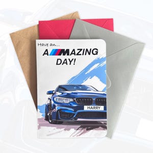 May include: A rectangular greeting card featuring a blue sports car illustration and the text "Have an... A-MAZING DAY!" with the BMW logo colours integrated into the word "AMAZING". The number plate displays the name "HARRY". Three envelopes are behind.