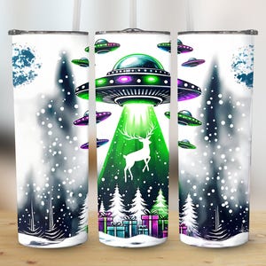 May include: Three white stainless steel tumblers with a Christmas-themed design. The design features a green and purple UFO with a green beam of light shining down on a white deer in a snowy forest. The tumblers are perfect for holding hot or cold beverages.