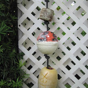May include: A vertical string of three nautical buoys suspended by a black rope. The top buoy is a weathered, textured cylinder. The middle buoy is a spherical shape with a red top and white bottom. The bottom buoy is yellow with the text X317.
