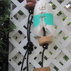 May include: A white foam lobster buoy featuring a horizontal teal stripe and the carved number 36. The buoy is attached to a black rope with two brown cylindrical cork floats at the top and one brown cylindrical cork float at the bottom.