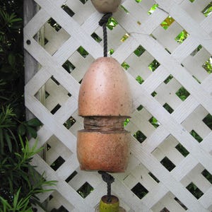 May include: A weathered, light brown, cylindrical lobster buoy made of two stacked foam sections, suspended by a black rope. The buoy features a smaller, rounded, tan top float and a smaller, green and grey bottom float, showing signs of wear.