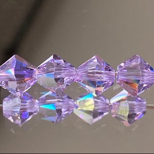 May include: A strand of iridescent purple faceted glass beads. The beads are shaped like a diamond with a pointed top and bottom.