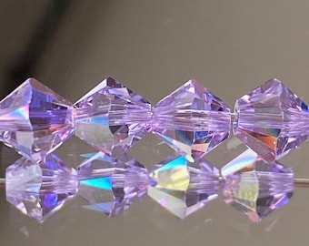 Può includere: Un filo di perline di vetro sfaccettate di colore viola iridescente. Le perline hanno la forma di un diamante con una parte superiore e inferiore appuntita.