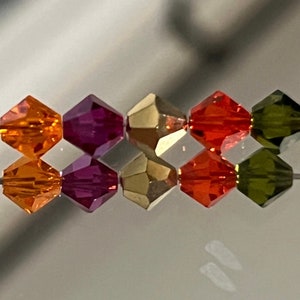May include: A strand of faceted glass beads in orange, purple, gold, and green colors. The beads are strung on a wire and are arranged in a repeating pattern.