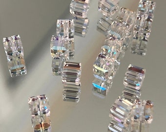 May include: A group of clear glass beads with a faceted, iridescent finish. The beads are scattered on a reflective surface.
