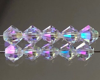 May include: A strand of iridescent clear glass beads with a faceted diamond shape. The beads are strung on a wire and are reflecting light.