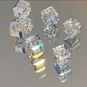 May include: A group of clear crystal beads with a faceted design. The beads are arranged in a cluster on a reflective surface.