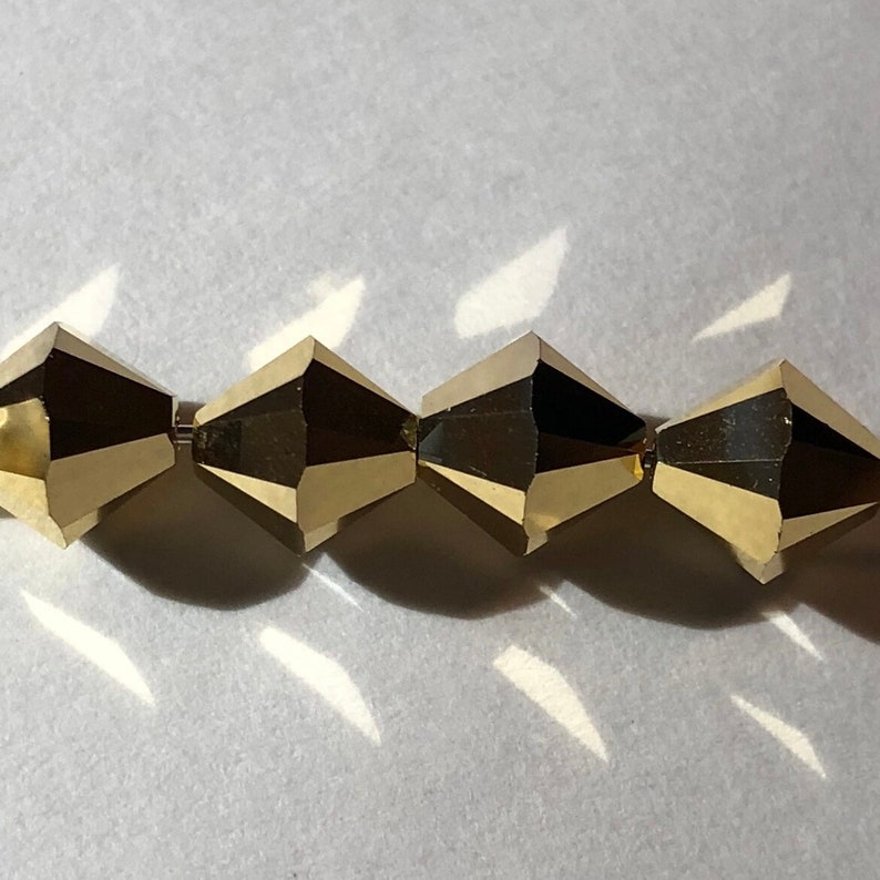 May include: A close-up of four gold-colored faceted beads. The beads are arranged in a row and are strung together.