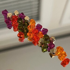 May include: A cluster of colorful glass beads in shades of orange, green, and purple. The beads are faceted and have a shiny finish.