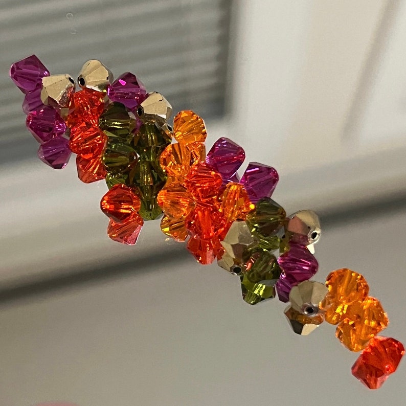 May include: A cluster of colorful glass beads in shades of orange, green, and purple. The beads are faceted and have a shiny finish.