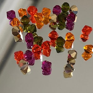May include: Assortment of colorful faceted glass beads in shades of red, orange, yellow, and green. The beads are various shapes and sizes, and have a shiny, iridescent finish.