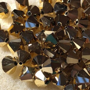 May include: A pile of gold-colored faceted glass beads. The beads are small and have a pointed shape.