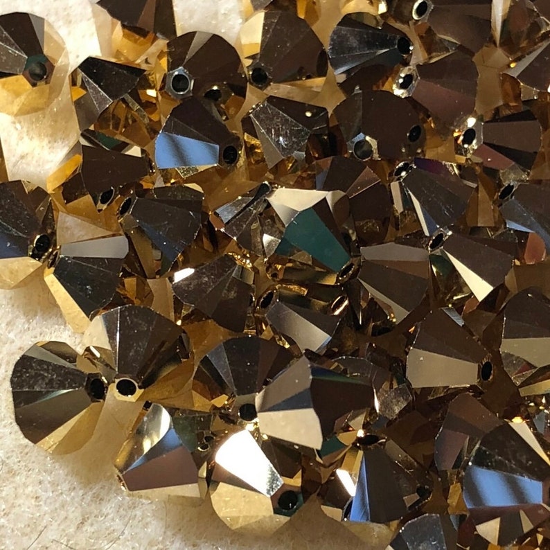 May include: A pile of gold-colored faceted glass beads. The beads are small and have a pointed shape.