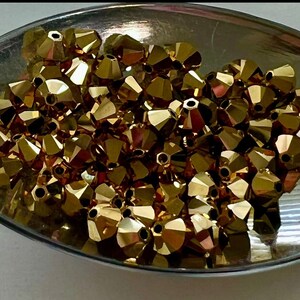 May include: A bowl filled with gold-colored faceted beads. The beads are small and have a shiny finish.