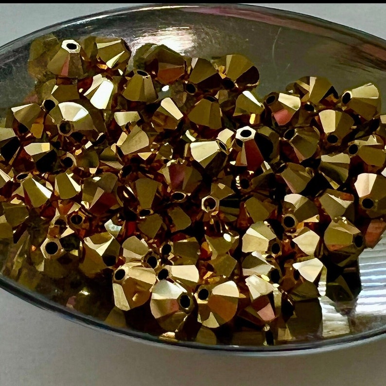 May include: A bowl filled with gold-colored faceted beads. The beads are small and have a shiny finish.