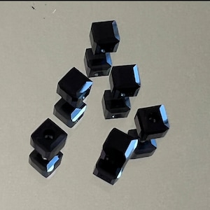 May include: A group of eight black cube-shaped earrings. The earrings are stacked on top of each other in a triangular shape.