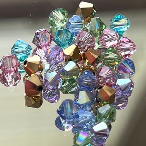 May include: A collection of faceted beads in various colors, including pink, green, blue, and gold. The beads have a shiny, iridescent finish, reflecting light. The beads are likely for jewelry making or other craft projects.