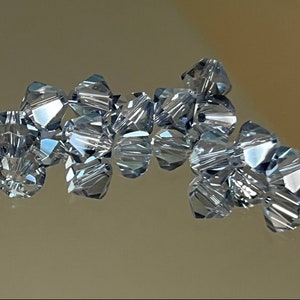 May include: A group of clear, faceted glass beads with a light blue tint. The beads are arranged in a loose cluster, with some overlapping.