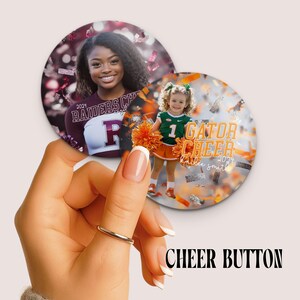 May include: Two round cheerleading buttons. One features a smiling young woman in a maroon Raiders cheerleading uniform. The other shows a young girl in a green and orange Gator cheerleading uniform. The text "CHEER BUTTON" is at the bottom.
