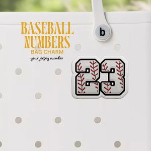 May include: White cooler with a baseball number 23 charm attached. The charm is white with red stitching and a baseball pattern. The text "Baseball Numbers Bag Charm your jersey number" is printed in yellow on the cooler.