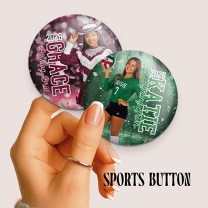 May include: Two circular pin-back buttons featuring personalized sports photography. One button shows a majorette in maroon and white with the text Grace 2026 Bulldog Drill. The other shows a volleyball player in green with the text Katie 2026 Fighting Irish.