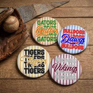 May include: Four circular pinback buttons featuring team names. One has orange and green text reading GATORS on a striped background. Another has red and blue text reading BULLDOGS and Dawgs. One has black and gold text reading TIGERS. One has maroon and gray text reading VIKINGS.