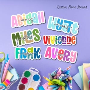 May include: Six custom name stickers featuring colorful, bold, bubble-style lettering with black cursive text overlays. The names Abigail, Wyatt, Miles, Vivienne, Frank, and Avery are displayed in various bright color combinations on a purple background.
