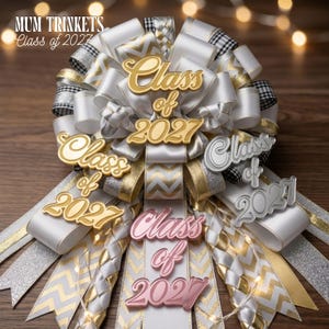 May include: A decorative homecoming mum featuring layered white, gold, and silver ribbons with chevron and plaid patterns. The accessory is adorned with multiple cut-out signs reading "Class of 2027" in gold, silver, and rose gold metallic finishes.
