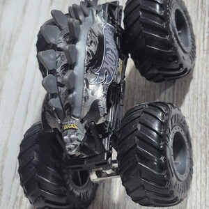 May include: A black and silver Hot Wheels Monster Truck with large, textured tyres. The truck features a detailed design with the Hot Wheels logo and the words "Monster Trucks". The truck has a spiked design on top.