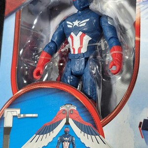 May include: A Captain America action figure in blue, red, and white tactical gear with a matching helmet and red gloves, encased in clear plastic packaging. The packaging features an illustration of the figure with large, detachable red and white wings.