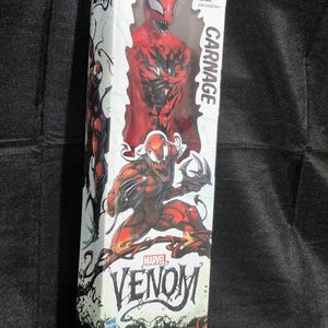 May include: A Carnage action figure from the Marvel Venom Titan Hero Series in its original white packaging. The box features red and black graphics of the character, the text Carnage, Marvel Venom, and Titan Hero Series, with an age 4+ label.