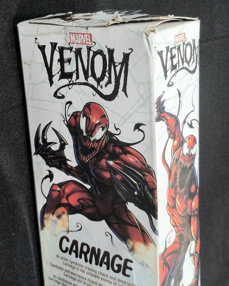 May include: A white rectangular cardboard box featuring Marvel Venom branding and a large illustration of the red and black Carnage character. The box displays the name Carnage in bold black text and includes descriptive text about the character.