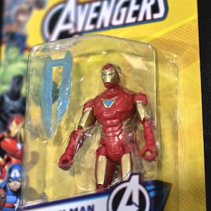 Puede incluir: Una figura de acci&oacute;n de Iron Man con armadura roja y dorada y un reactor arc azul en el pecho, dentro de un empaque de pl&aacute;stico transparente sobre una tarjeta amarilla de la marca Marvel Avengers. Incluye un accesorio azul transl&uacute;cido.