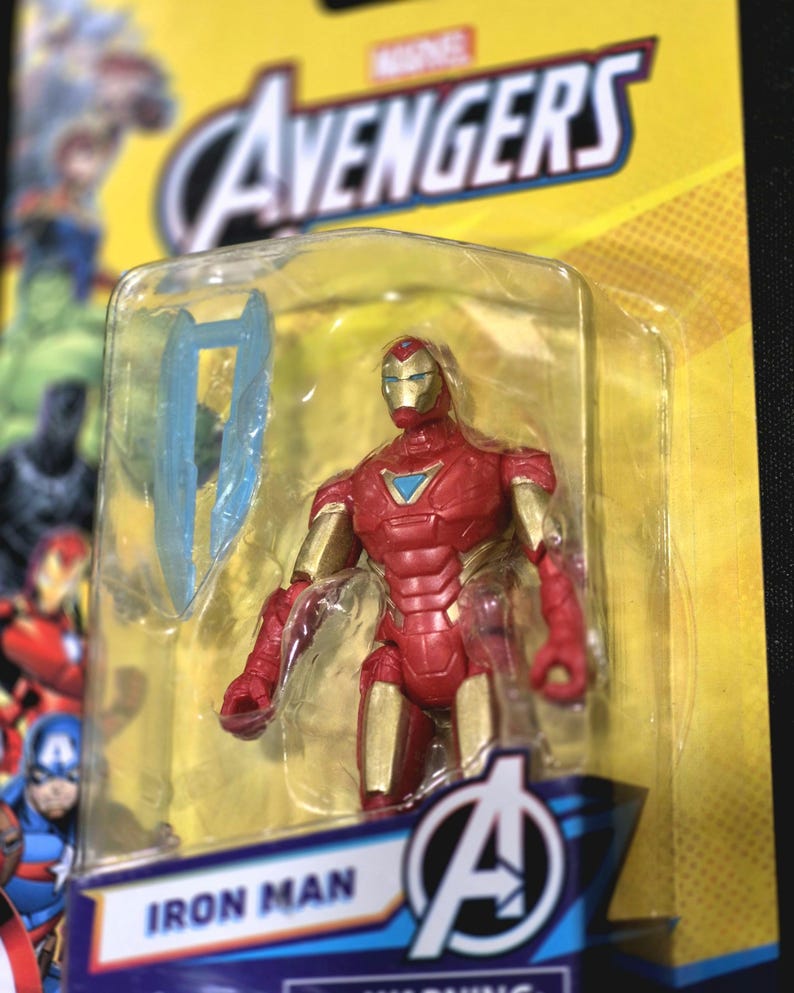 Puede incluir: Una figura de acci&oacute;n de Iron Man con armadura roja y dorada y un reactor arc azul en el pecho, dentro de un empaque de pl&aacute;stico transparente sobre una tarjeta amarilla de la marca Marvel Avengers. Incluye un accesorio azul transl&uacute;cido.