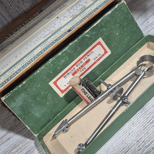 May include: A vintage Minusa Bow Pencil compass set in a green box with a red and white label. The set includes a compass, fine lead, and a Reynolds Metals Company aluminum slide rule. The compass is 5.5 inches long.