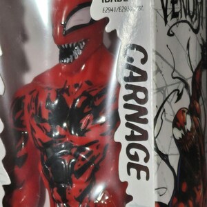 May include: A red and black Carnage action figure inside its original packaging. The box features the Marvel Venom logo, the text Carnage, and age rating information. The figure has a detailed muscular physique with black vein-like markings.