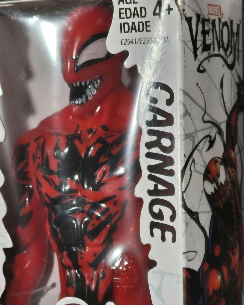 May include: A red and black Carnage action figure inside its original packaging. The box features the Marvel Venom logo, the text Carnage, and age rating information. The figure has a detailed muscular physique with black vein-like markings.