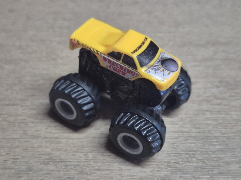 A yellow and black toy monster truck with large black tires. The truck has the words "WRECKING CREW" on the side and the website "BANGING.COM" on the roof.