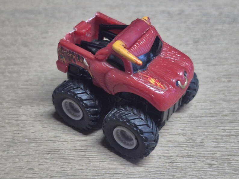 A red toy monster truck with black tires and white rims. The truck has yellow horns and a bull-like design on the front. The text "Toro Loco" is visible on the side.