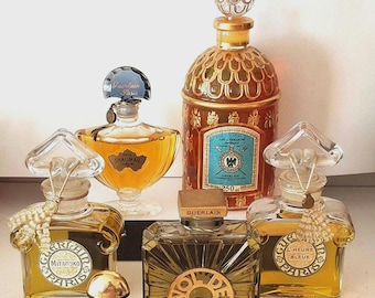 May include: A collection of six Guerlain perfume bottles of varying shapes and sizes. The set includes clear glass bottles with heart-shaped stoppers, a tall cylindrical bottle with a gold scale pattern, and a dark red bottle with a gold cap.