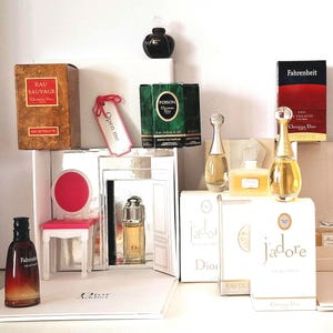 Puede incluir: Una colección de productos de fragancia Christian Dior que incluye varios frascos de perfume y cajas. Los artículos destacados incluyen aromas de Eau Sauvage, Poison, Fahrenheit y J'adore, junto con una silla miniatura blanca y rosa y una etiqueta que dice Open me.