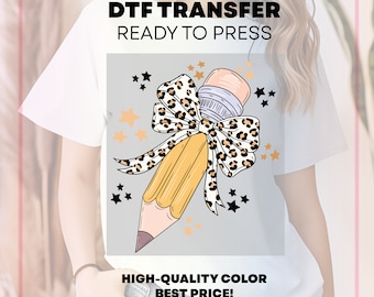 May include: White t-shirt featuring a pencil design with a leopard print bow, surrounded by stars. The text "DTF TRANSFER READY TO PRESS" and "HIGH-QUALITY COLOR BEST PRICE!" are displayed. This graphic tee is perfect for school or teacher-themed designs.