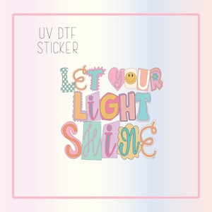 May include: UV DTF sticker with the text "Let your light shine" in colorful, outlined letters. The letters are decorated with hearts, flowers, and a smiley face.