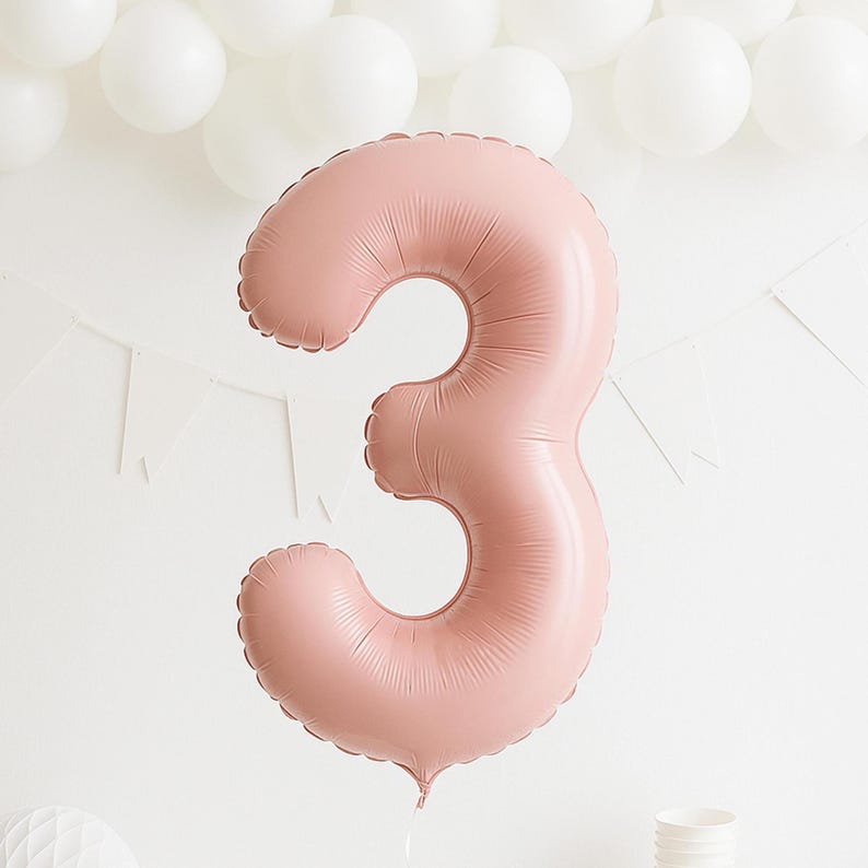 May include: A large, pink number 3 balloon, perfect for a third birthday. The balloon is inflated and has a matte finish. White balloons and a banner are in the background.