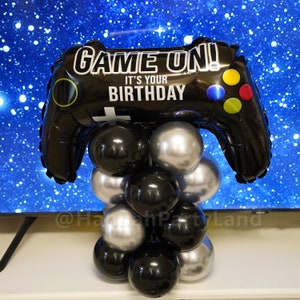 May include: A black and silver balloon centrepiece shaped like a video game controller with the text "Game On! It's Your Birthday".