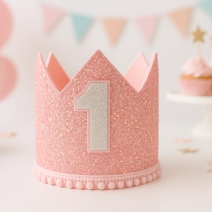 May include: Pink felt crown with a white felt number one on the front. The crown is decorated with pink glitter and has a white felt trim around the bottom.