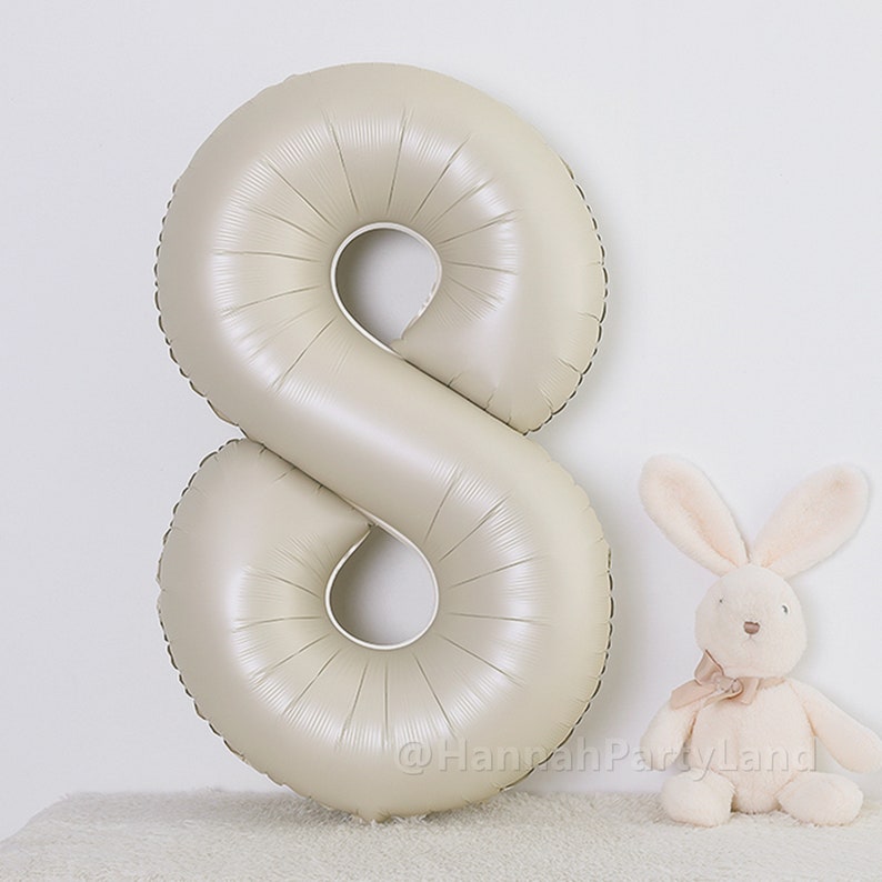 May include: A large, beige, foil number eight balloon. The balloon is inflated and ready to be used for a party or celebration.