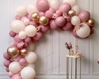 Pode incluir: Um arco de balões feito de balões rosa claro, brancos e dourados. O arco é decorado com pequenas flores cor-de-rosa. O arco está instalado em frente a uma parede branca com moldura branca.