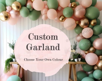 May include: A custom garland made of green and pink balloons with gold accents. The garland is hanging on a white wall and is decorated with greenery. The text "Custom Garland" and "Choose Your Own Colour" is written on a pink background.